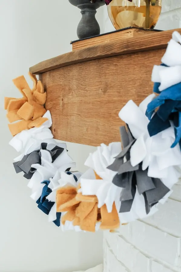 a garland of one inch strips of felt tied around a string. it looks like one long pom pom with sections of orange, white, grey, and navy blue.